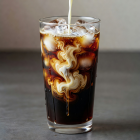Cold brew coffee over ice in a tall glass with milk swirling